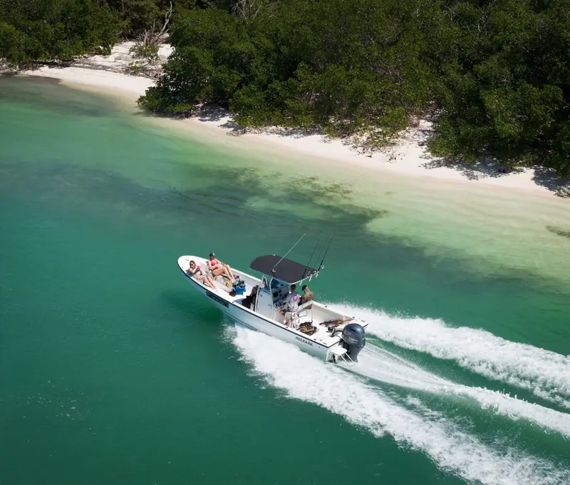 A centre-console boat with fishing rods running past a mangrove-lined sandbar in shallow turquoise water